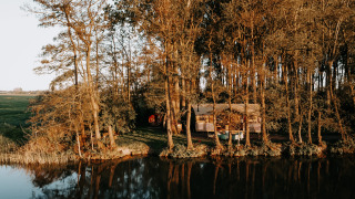 The Glamphuys Ultra Wellness safari tent is nestled among trees by a calm lake, surrounded by nature.