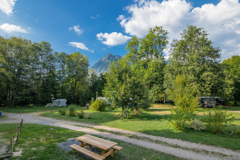 Zicht op Onlycamp Camping Les Thézières met groene bomen, bergen op de achtergrond en een picknicktafel.