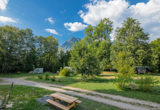 Blick auf Onlycamp Camping Les Thézières mit Bäumen, Wiese, Bergen im Hintergrund und Picknicktisch.