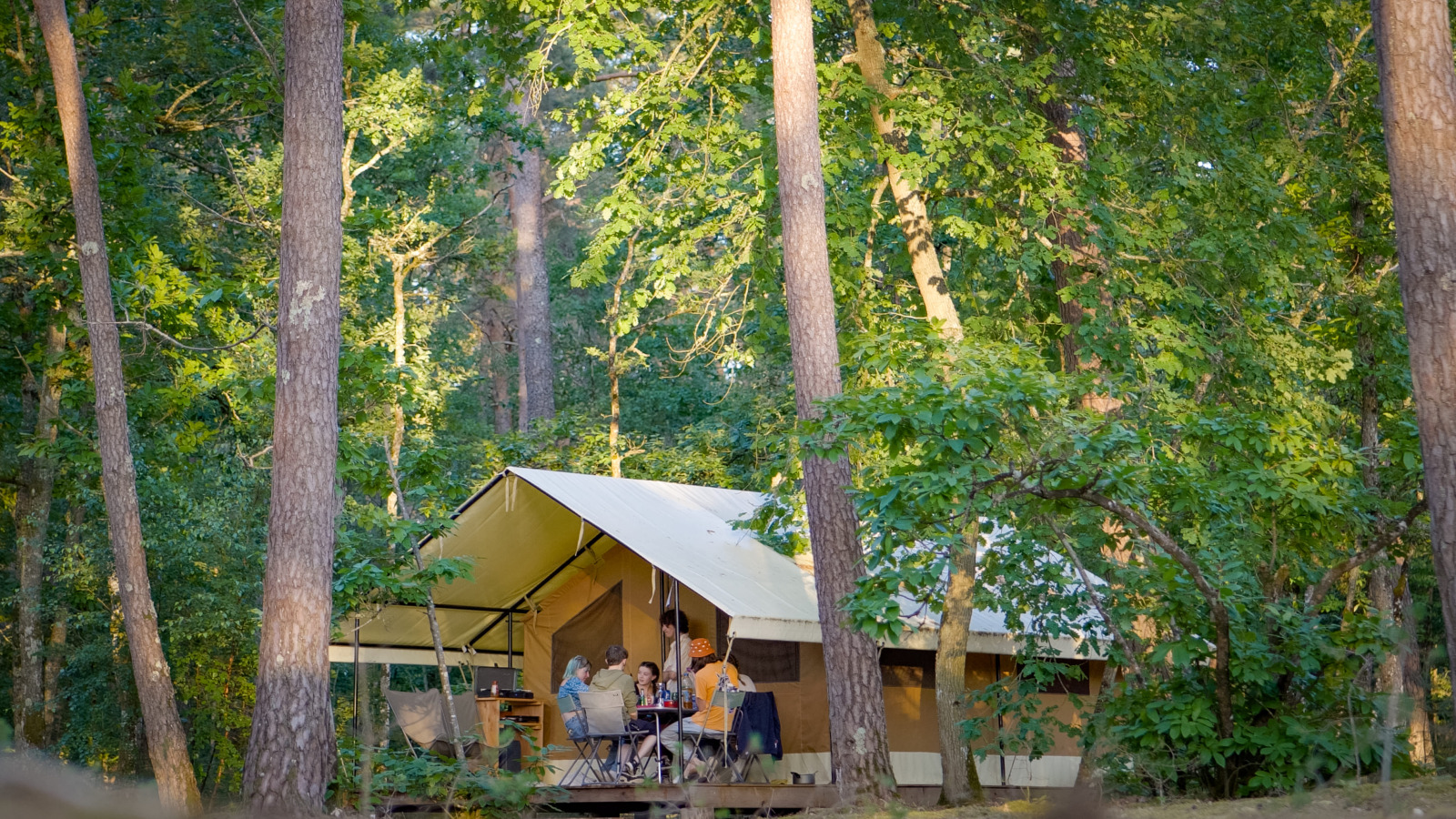 Interieur van een glampingtent met eettafel, stoelen, kitchenette, koelkast en twee aparte bedden.
