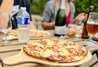 Buiten tafelen met pizza en drank aan Camping Vauban, Grand Est, Frankrijk.
