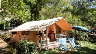 Ponza safaritent met open voortent, stoelen en parasol, gelegen tussen groene bomen en natuur.