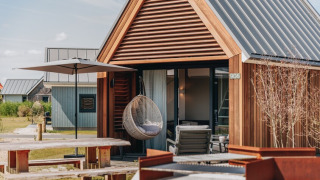 Tiny wooden house with a hanging chair, umbrella, picnic table, and fire pit in front of Tiny House 2.
