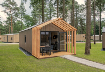 Tiny House 2, a compact wooden cabin with open porch and seating, set in a peaceful, forested area.