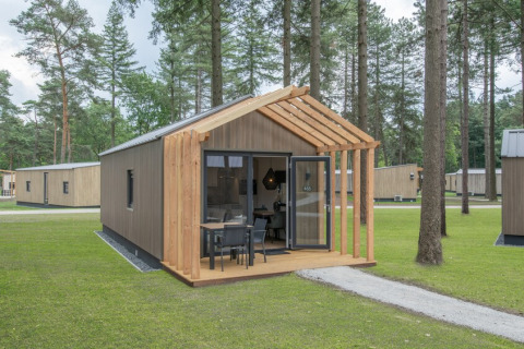 Tiny House 2, piccola casa in legno con veranda e sedie all'aperto, immersa in una zona boschiva.