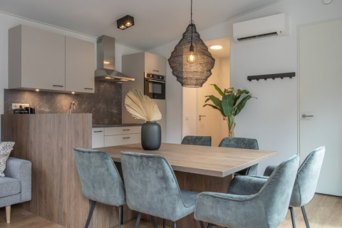 Modern dining and living area with wooden table, velvet chairs, and open kitchen in Timber Cottage 6.
