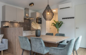 Moderne opholds- og spiseområde med stilfulde stole, træbord og et åbent køkken i Timber Cottage 6.