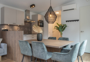 Moderne opholds- og spiseområde med stilfulde stole, træbord og et åbent køkken i Timber Cottage 6.