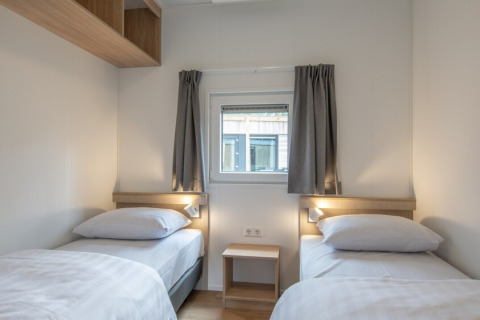 Et lyst værelse i Timber Cottage 6 med to enkeltsenge, vindue og minimalistisk indretning i Bospark 't Wolfsven.