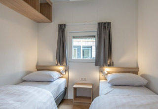 Et lyst værelse i Timber Cottage 6 med to enkeltsenge, vindue og minimalistisk indretning i Bospark 't Wolfsven.