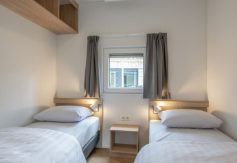 Et lyst værelse i Timber Cottage 6 med to enkeltsenge, vindue og minimalistisk indretning i Bospark 't Wolfsven.