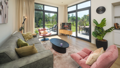 Woonkamer van lodge ‘Cannenburch’ Deluxe in Veluwe park de Bosgraaf, Nederland, met modern interieur en tuinzicht.