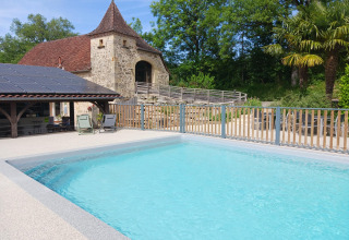 Buitenzwembad met historisch stenen gebouw bij Domaine Papillon vakantiepark in Occitanië, Frankrijk.