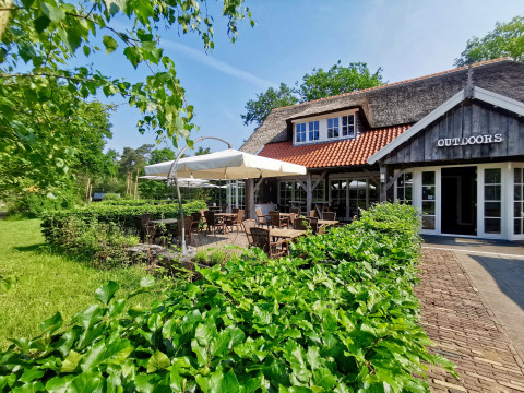 Buitenzitje aan Outdoors Holten vakantiepark in Overijssel, Nederland, met veel groen en gezellig terras.