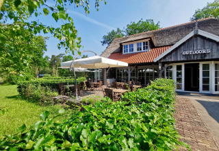 Buitenzitje aan Outdoors Holten vakantiepark in Overijssel, Nederland, met veel groen en gezellig terras.