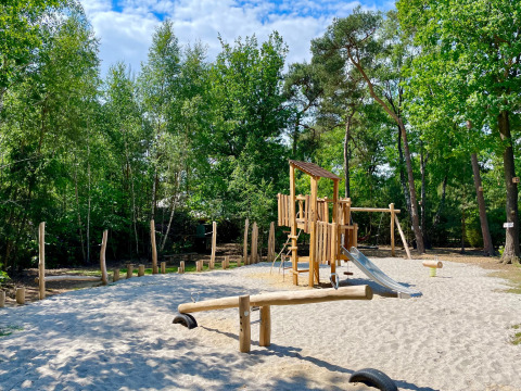 Speelplein met houten klimrek en glijbaan in Outdoors Holten vakantiepark, omgeven door bos in Overijssel.