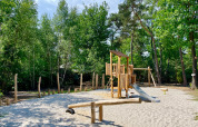 Spielplatz mit Holzgeräten und Rutsche im Ferienpark Outdoors Holten, umgeben von Wald in Overijssel.