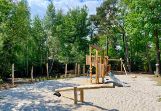 Speelplein met houten klimrek en glijbaan in Outdoors Holten vakantiepark, omgeven door bos in Overijssel.