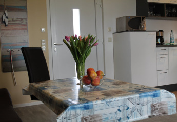 Dining area at 'Am Strand' lodge in Germany, featuring a vase of flowers and bowl of fruit on the table.