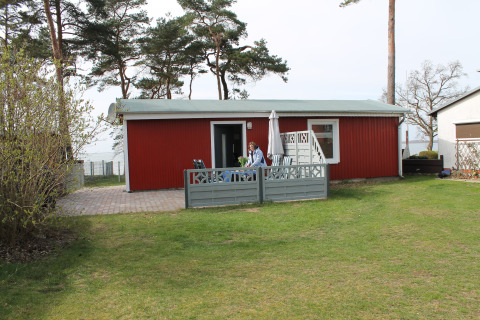 Red lodge at Am Strand in Germany with patio, garden furniture, and a person sitting outside.