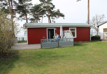 Red lodge at Am Strand in Germany with patio, garden furniture, and a person sitting outside.