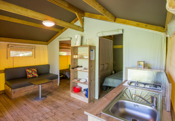 Indvendig udsigt over Freeflower Comfort safaritelten på Flower Camping Le Pont du Tarn med køkken og sofa.