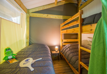 Indvendigt billede af et safaritelt med køjeseng og enkeltseng på Flower Camping Le Pont du Tarn i Frankrig.