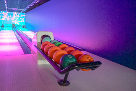 Bowlingbahn mit bunten Kugeln im Regal und Neonbeleuchtung in einer Lodge am Abend aufgenommen.