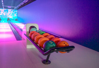 Bowlingbane med farverige kugler på stativ og neonlys, der oplyser banen på en lodge om aftenen.