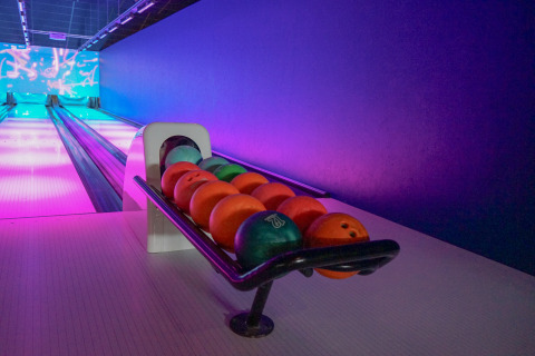 Bowling alley with colorful balls on a rack and neon lighting, taken at a lodge in the evening.