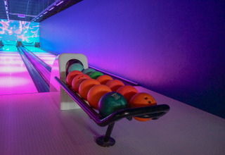 Bowling alley with colorful balls on a rack and neon lighting, taken at a lodge in the evening.
