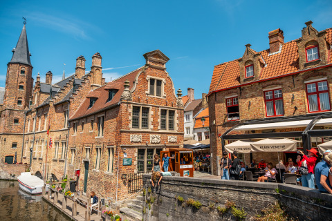 Photo d’un canal pittoresque, de bâtiments historiques en briques et de terrasses animées par une journée ensoleillée.