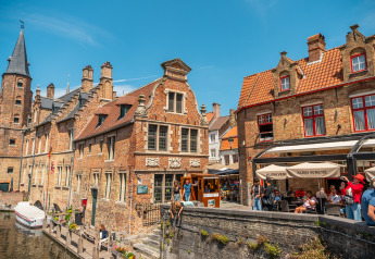 Photo d’un canal pittoresque, de bâtiments historiques en briques et de terrasses animées par une journée ensoleillée.