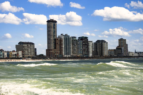 Hochhäuser und Apartments an der Küste mit Wellen und blauem Himmel, vom Wasser aus am Tag gesehen.