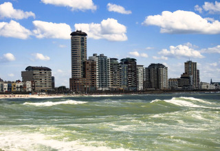 Immeubles et appartements en bord de mer, avec vagues et ciel bleu, vus de l’eau en journée.