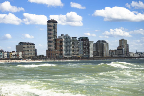 Tall buildings and apartments along the coastline, with waves and blue sky, viewed from the water by day.