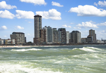 Immeubles et appartements en bord de mer, avec vagues et ciel bleu, vus de l’eau en journée.