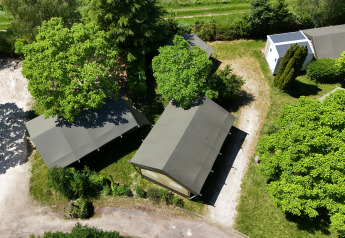 Luchtfoto van een safaritent op een camping, omgeven door groene bomen en zonnige wandelpaden.