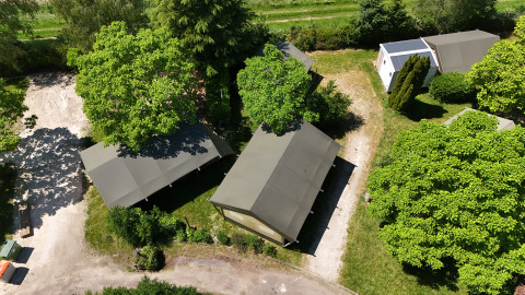 Vista aerea di una tenda safari in campeggio, circondata da alberi verdi e sentieri soleggiati.