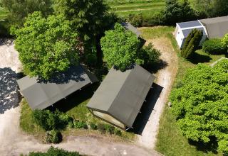 Aerial view of a safari tent on a campsite, surrounded by lush green trees and sunny footpaths.
