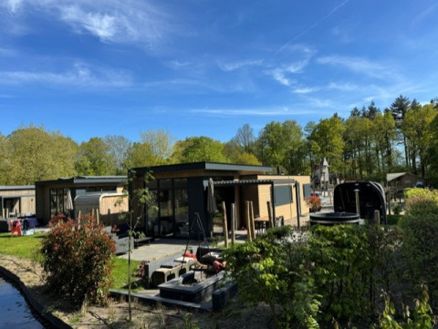 Buitenzicht op de Cannenburch Deluxe lodge met hot tub, sauna, terras en omgeven door groen en bos.