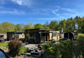 Vue extérieure du lodge Cannenburch Deluxe avec bain à remous privé, sauna et terrasse moderne entourée de verdure.