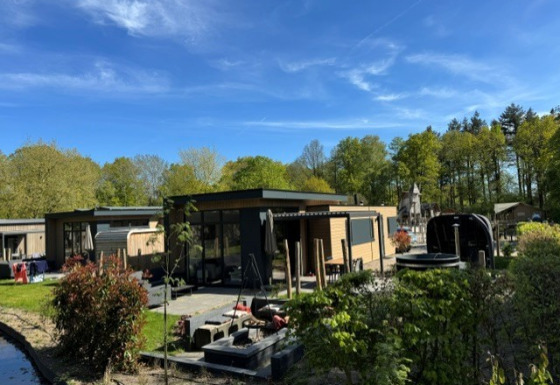 Buitenzicht op de Cannenburch Deluxe lodge met hot tub, sauna, terras en omgeven door groen en bos.