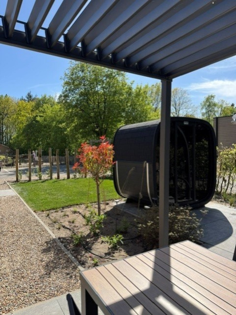 Terrasuitzicht met moderne pergola, tuin en podvormige lodge bij Veluwe park de Bosgraaf, Nederland.