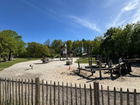 Speelplaats met zand en houten toestellen te Veluwe park de Bosgraaf, Nederland, onder een blauwe lucht.
