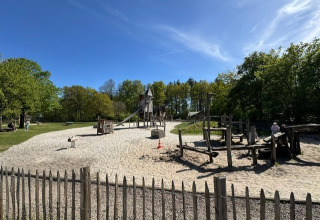 Speelplaats met zand en houten toestellen te Veluwe park de Bosgraaf, Nederland, onder een blauwe lucht.