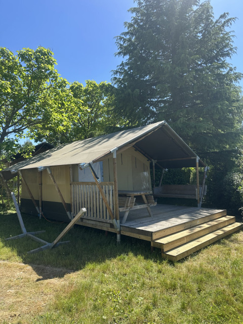 Safari tent named Compact with private sanitary facilities, wooden terrace, and picnic table outdoors.