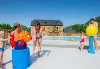 Famiglia che gioca con giochi d’acqua accanto alla piscina, casa in pietra e colline sullo sfondo.