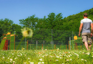 Uomo che cammina tra i fiori vicino a un parco giochi al Seasonova Camping Les Rives d'Olt et Aubrac in Francia.