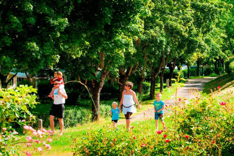 Famiglia che passeggia in un parco verde con alberi a Seasonova Camping Les Rives d'Olt et Aubrac, Occitanie, Francia.